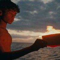 Boy without shirt holds plate with oil candle