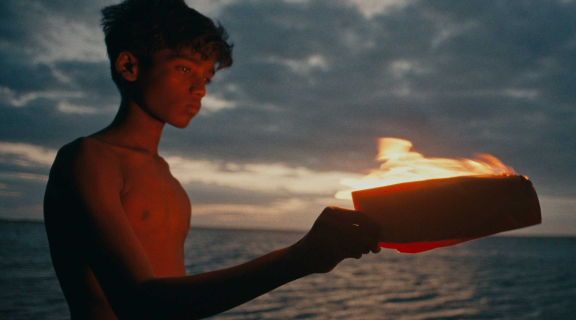Boy without shirt holds plate with oil candle